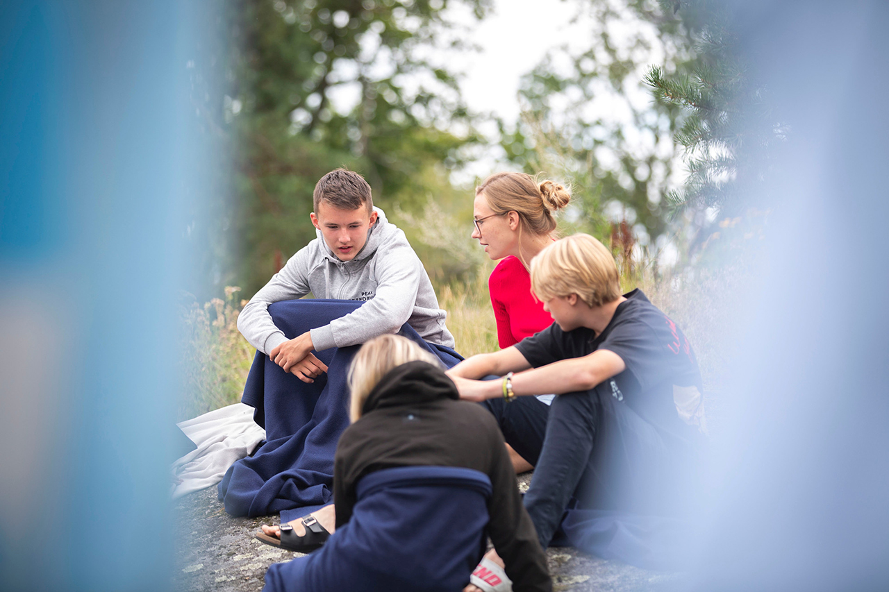 sportscamp_konda Ungdomar sitter och pratar. Klädda i idrotts eller friluftskläder och med filtar att värma sig med.